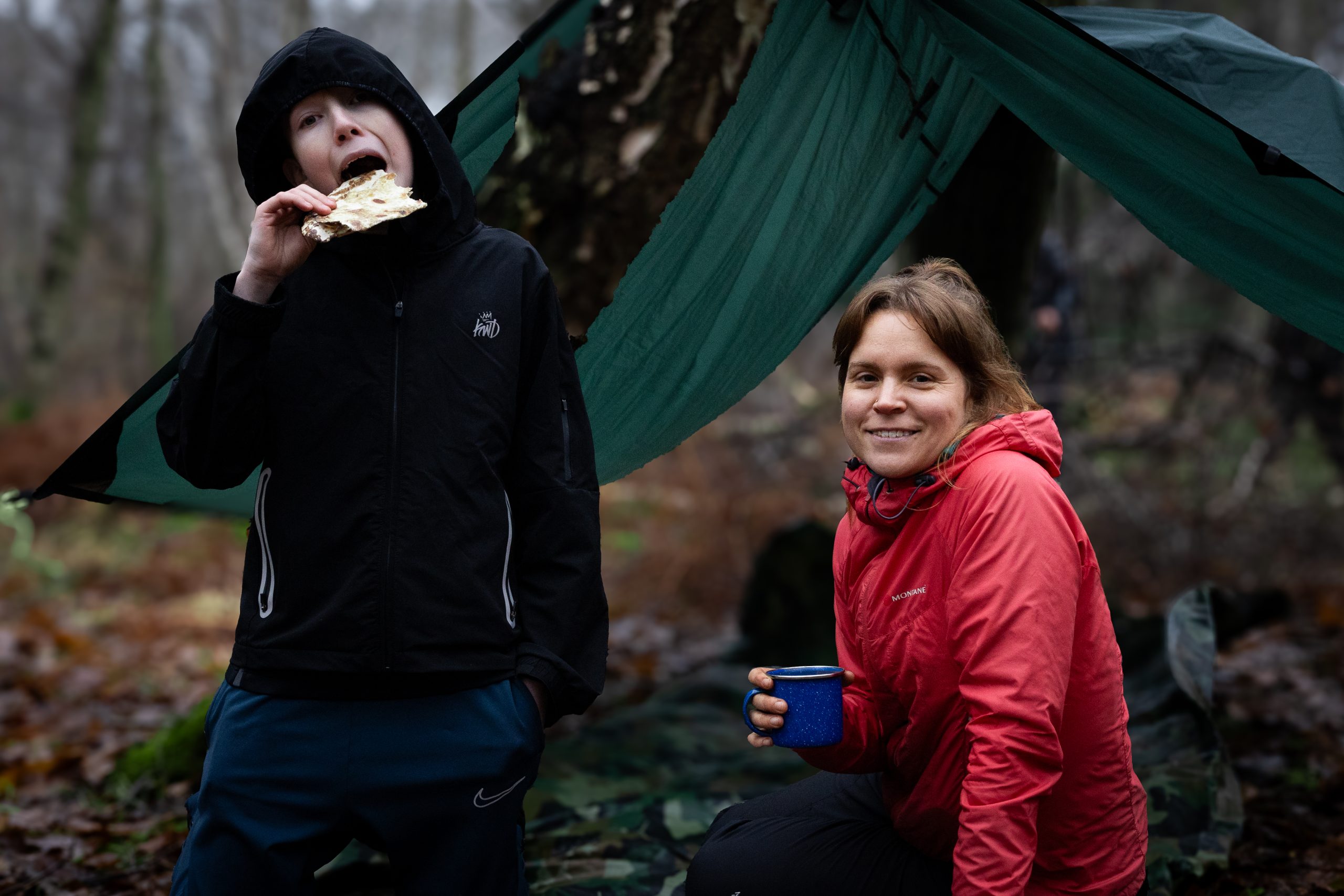 Young person eating next to a tarp in the woods